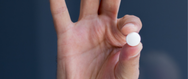man holding a round pill between his thumb and pointer finger