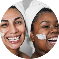 Two women with skin care products on their cheeks smile