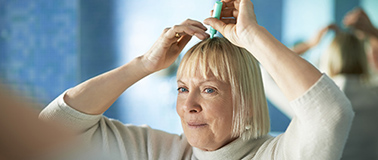img title A woman applying a topical treatment to her scalp.